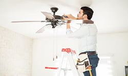 Attractive young handyman stepping on a ladder and fixing a ceiling fan Electrician El Dorado Hills